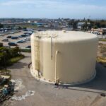 Drone photo of a large, off-white storage tank with the skyline in the background.