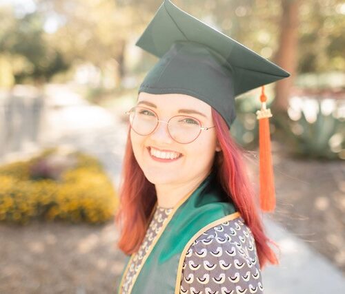 A smiling woman with a green graduate sash and cap from Cal Poly SLO University.